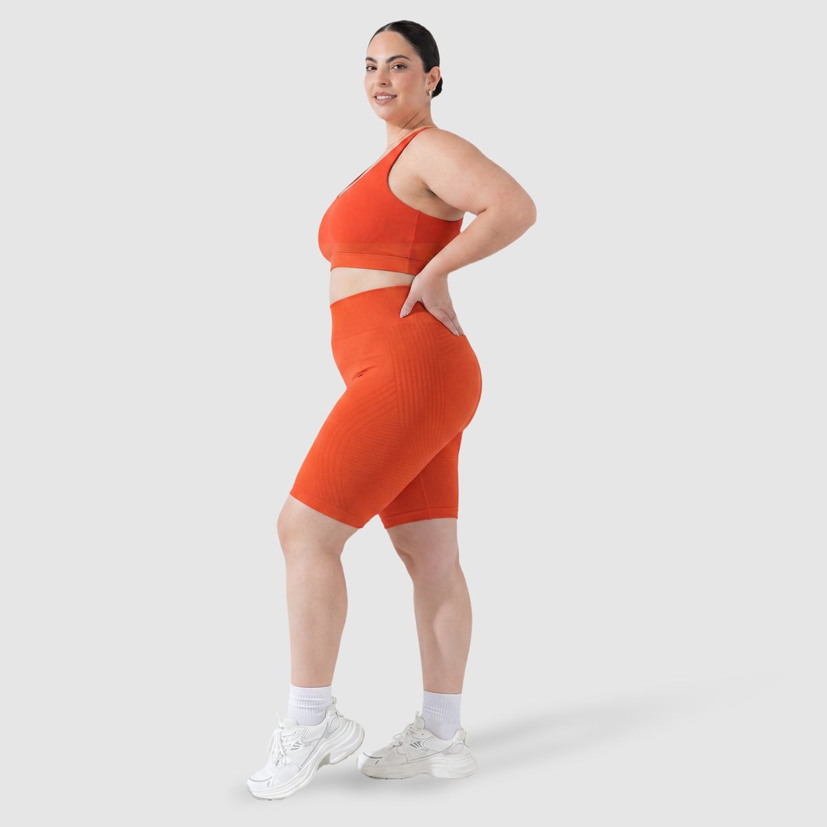 Kvinna i Sculpt 3D™ anticellulitshorts i orange, från sidan, med de formande 3D-linjerna synliga